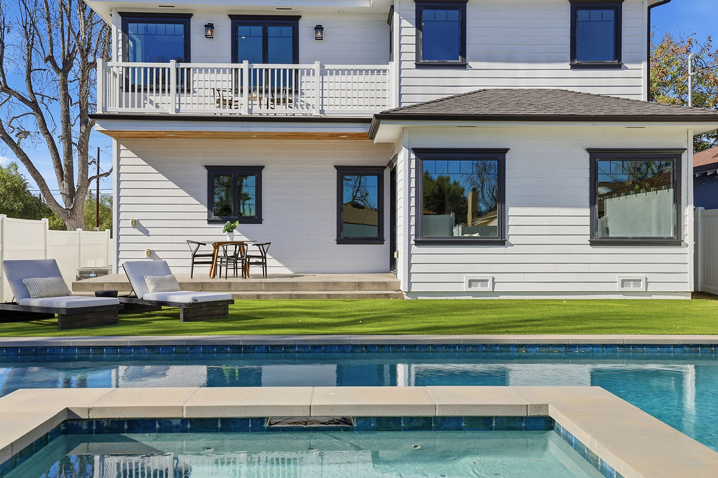 Backyard pool and spa beside a white two-story home with a balcony
